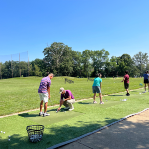 Tee It Up adult golf class at Reston National Golf Course driving range, with instructor providing one-on-one golf swing coaching to a student.