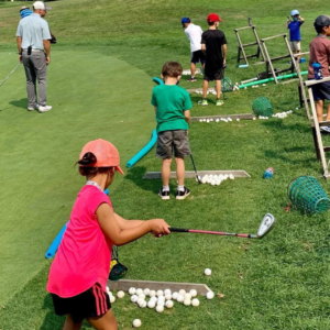 Junior golf camp at Reston National Golf Course practice green, with young golfers learning chipping techniques under instructor guidance.