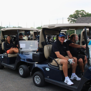Foursome of golfers riding in a golf cart at Reston National Golf Course, driving to the first hole to start a tournament round, enjoying the course and camaraderie.