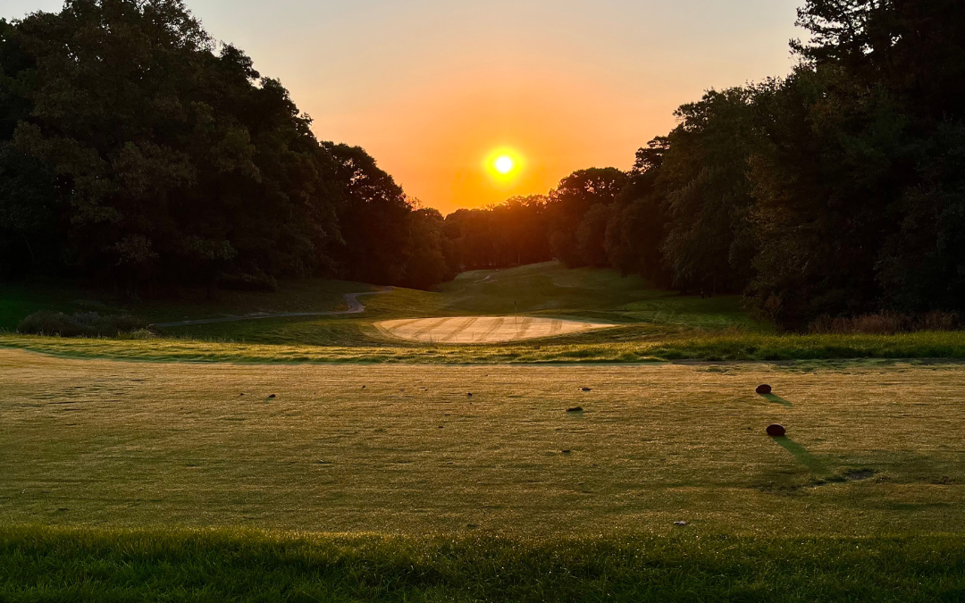 Sunrise over a tee box at Reston National Golf Course, casting warm light on the fairway and creating a serene morning golf scene.